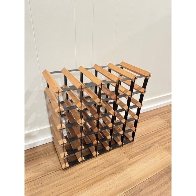 Sculptural modern wine rack featuring solid wood slats set within a black metal grid frame. This architectural design...