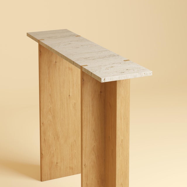 Two materials, one line. The Maha is a slim, upright table made to sit against a wall, its travertine surface carried on a...