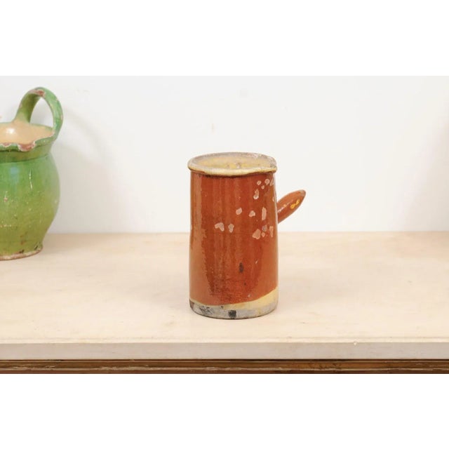 A French rustic pitcher from the 19th century, with rust colored glaze and straight handle. Created in France during the...