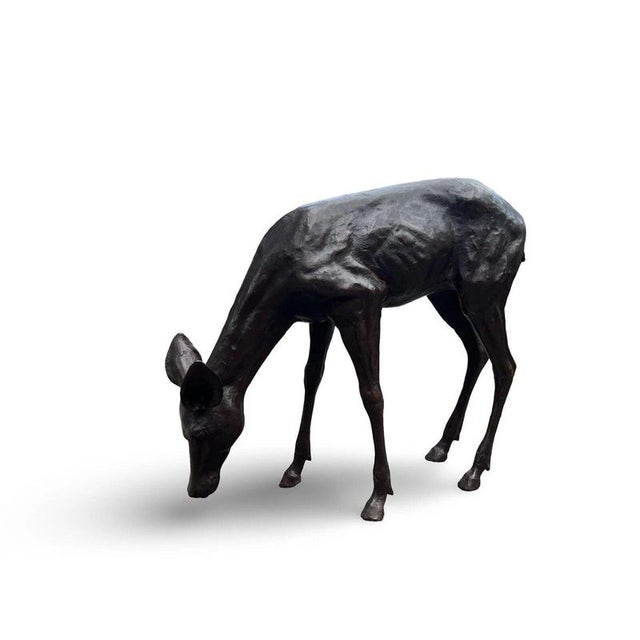 A charming bronze sculpture depicting a young deer grazing, beautifully modelled in a naturalistic and peaceful pose. with...