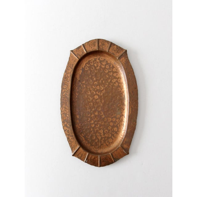 This vintage hammered copper tray by Schaefer features a richly textured surface framed by a segmented oval rim. The warm...
