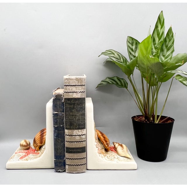 A pair of vintage ceramic bookends featuring sculpted scallop and spiral shells, pink starfish, coral, and seaweed against...
