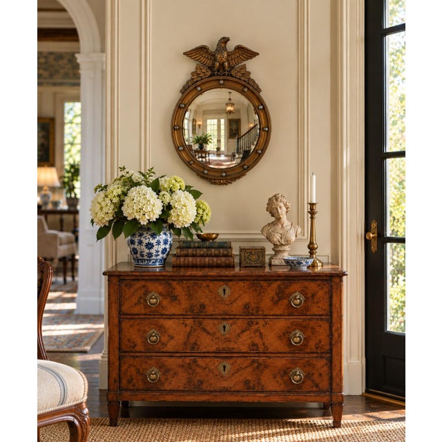 A Federal-style giltwood convex mirror crowned with a carved eagle, its wings outstretched above a laurel motif—an...