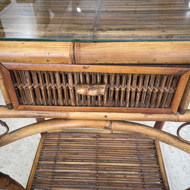 This is a mid-century modern rattan and bamboo console table with a glass top, drawer on a center, attributed to the style...