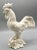 A Mid 20th-Century Italian blanc de chine rooster figurine perched upon a bunch of grapes and leaves, It is fine,...