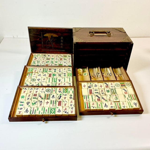 This is a lovely antique Mahjong Game Set. It features tiles that have bamboo backs with bone fronts. The tiles are...