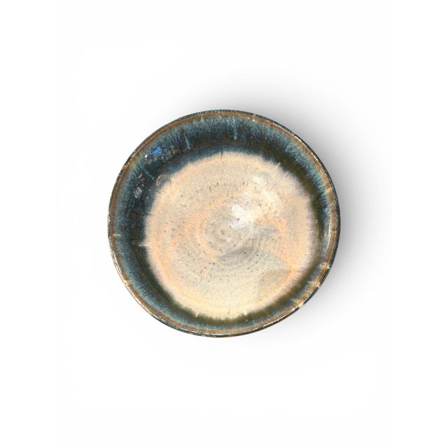 A glazed ceramic bowl by Gene Farkus, designed with a low footed base and wide flared form. The piece features a richly...
