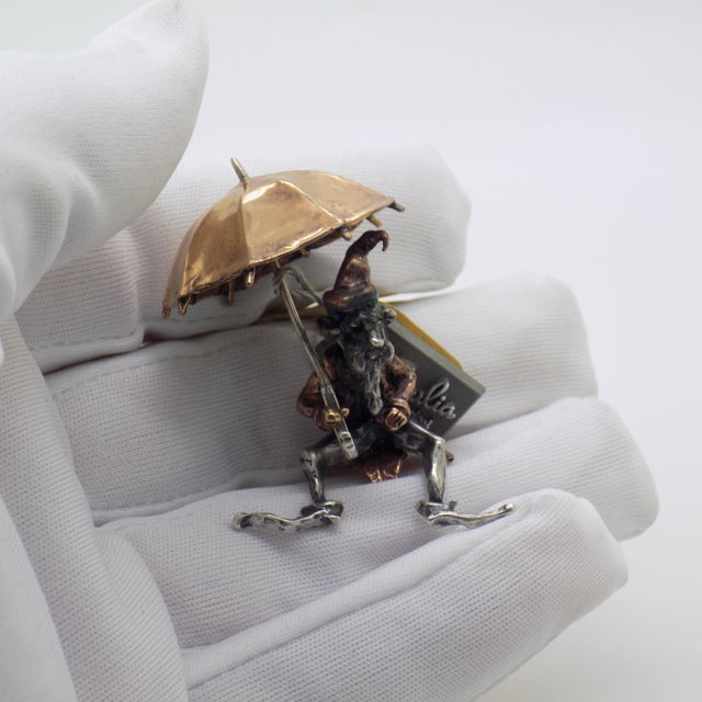 This vintage silver decorative object depicts an old goblin figure with an umbrella, crafted as a cabinet curiosity or...