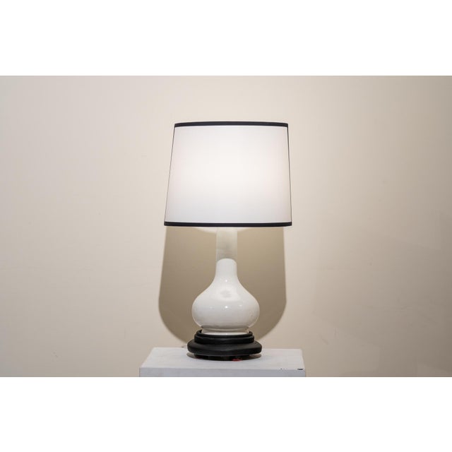 A 1960s vase table lamp. The structure consists of, from bottom to top, a circular, molded black wooden base and a...