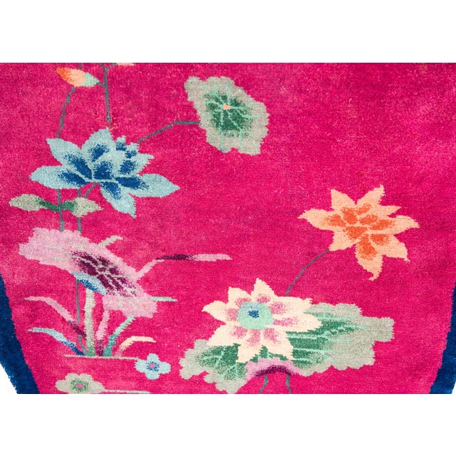 A rare early 20th century oval Art Deco rug with a thin indigo border surrounding a fuchsia field covered in multi-colored...