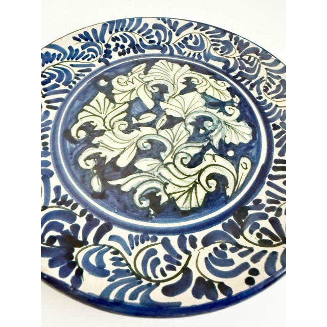 Handmade and hand-painted wall hanging ceramic plate decorated with traditional Hungarian floral motifs in blue and off-...