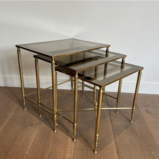 This set of three neoclassical-style nesting tables is made of brass with glass shelves surrounded by a line of silver-...