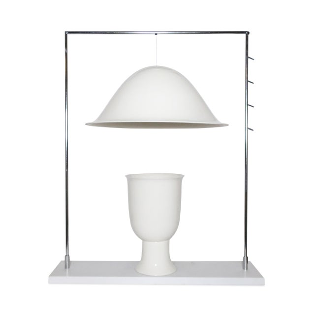 A striking object staged inside its own architecture. A chrome frame rises from a white Corian plinth in a single squared...