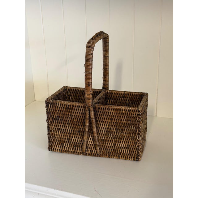 A beautifully handwoven rattan carrying caddy featuring a classic rectangular form with two divided compartments and a...