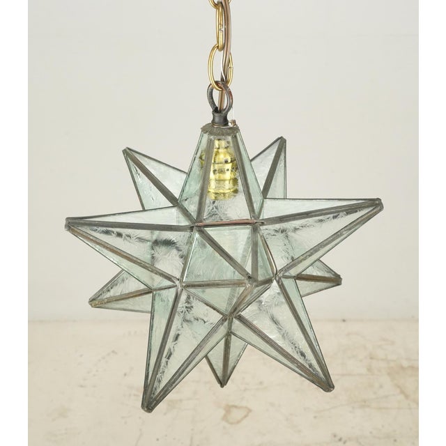 Modern style pendant light with a Moravian star shape with clear textured glass panels with welded seams. The chain is...