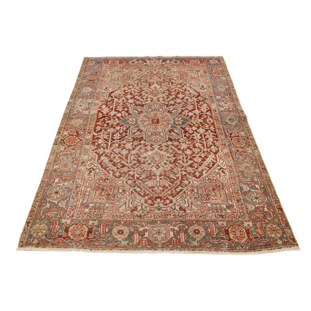 This hand-knotted Persian Heriz wool rug has a red field with blue and peach accents all over the medallion design. This...