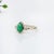 This ring showcases a striking 1.31 carat pear-shaped Emerald gemstone, flanked by two sparkling natural earth mined...