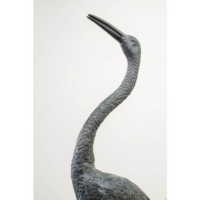 A pair of bronze sculptures in the round depicting a pair of herons. One stands with its neck erect and beak open towards...