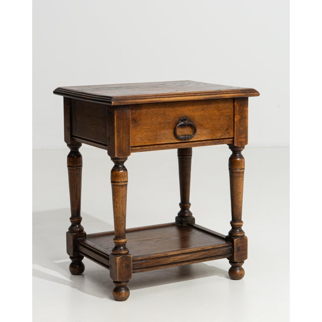 An oak side table featuring visible wood grain and a compact form. The design is simple with a slightly rustic character....
