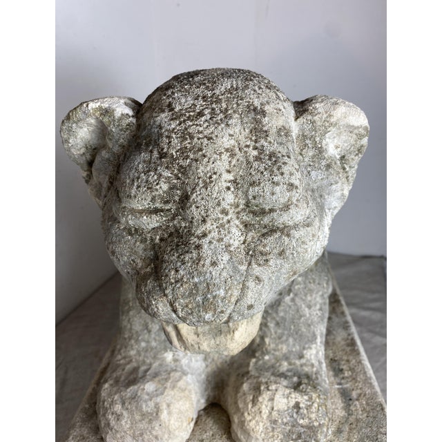A stone sculpture depicting a seated lion in a naive style, characterized by simple lines and massive forms. These cubic...
