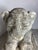 A stone sculpture depicting a seated lion in a naive style, characterized by simple lines and massive forms. These cubic...