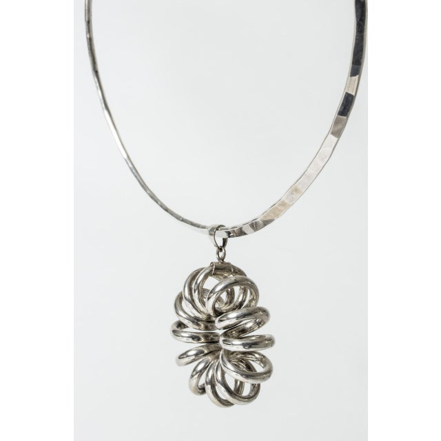 Eye-catching silver neckring by Göran Kuhlin, in a vivacious design with a spiraling pendant. Hammered finnish on the...