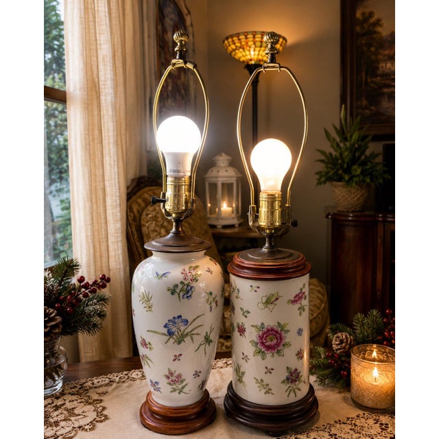 pair of vintage Chinoiserie porcelain table lamps with hand-painted floral motifs and wooden bases. • Left Lamp: Features...