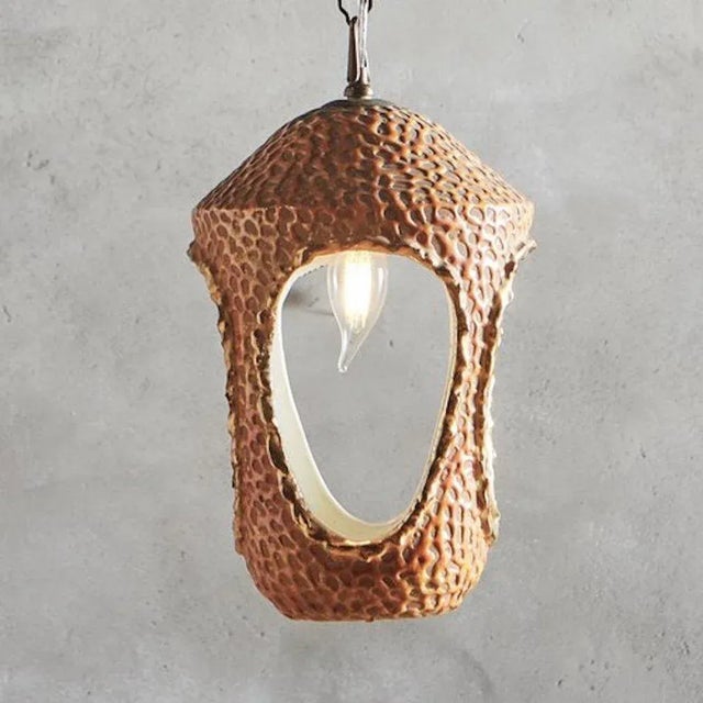 A 1950s glazed ceramic pendant light with oval cutout details on the sides and base. This fixture has gold detailing and a...
