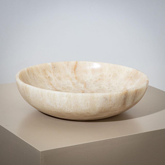 A large, heavy stone bowl made from beige onyx, designed in a minimalist style. The bowl is distinguished by its gently...