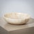 A large, heavy stone bowl made from beige onyx, designed in a minimalist style. The bowl is distinguished by its gently...
