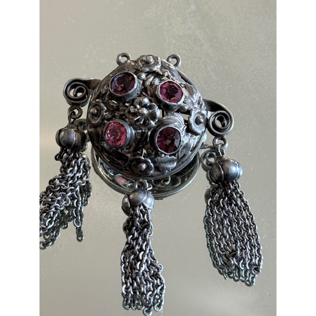 This vintage Art Nouveau Revival tassel brooch features a circular floral medallion with raised repoussé detailing,...