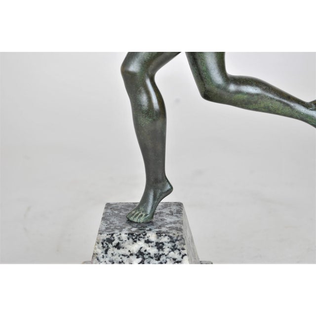 Bronze with a green patina of a young woman taking a swing to throw a ball The black and white granite base is signed Le...