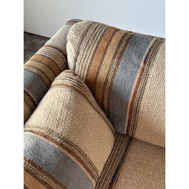 Wrapped entirely in richly textured striped upholstery, this vintage sofa carries a low, architectural silhouette with a...