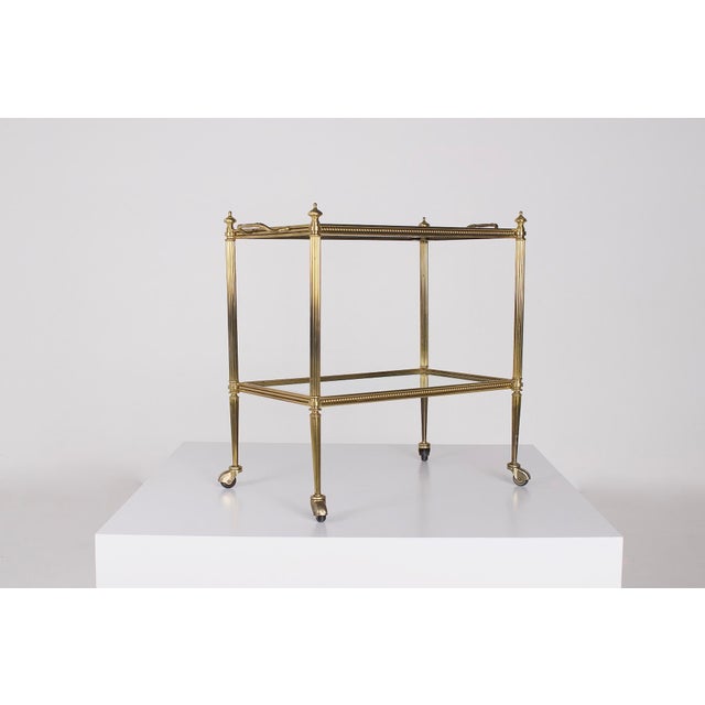 Neoclassical serving cart or bar trolley in solid brass, equipped with two glass shelves adorned with a mirrored border....