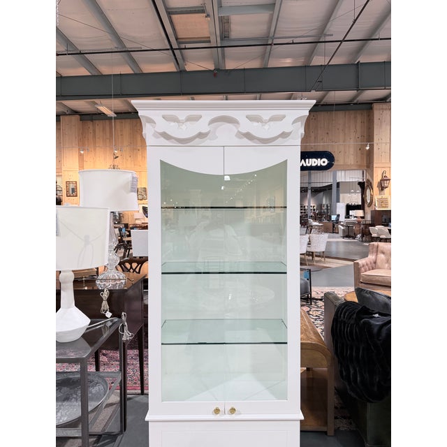 White painted curio cabinet featuring tall glass paneled doors, interior display shelves, and a decorative crown with...