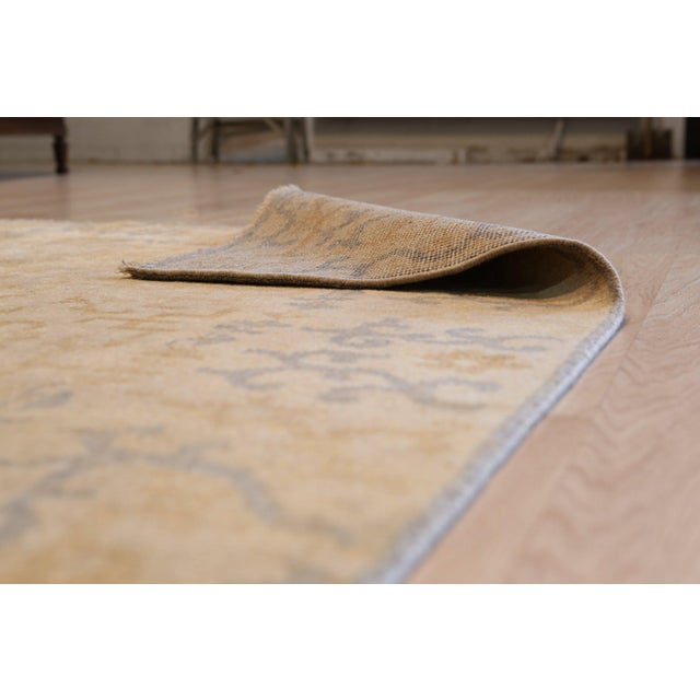 A 6' x 9' hand-knotted wool rug with a gold field with a faded gray-blue vine pattern and a soft, vintage-look finish....