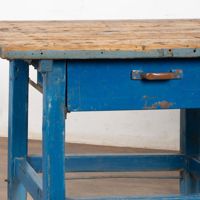 Rustic pine work table with base in old blue paint and two large metal drawers. The natural wood top bears deep gouges,...