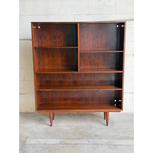 This beautiful open-face Bookcase displays a minimalist tall silhouette raised on round tapered legs. The architectural...