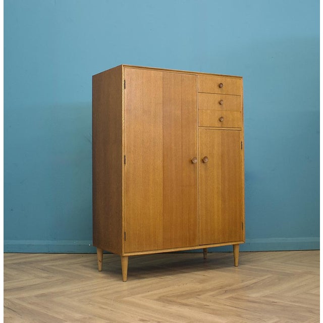 Compact mid-century wardrobe in oak by Meredew. Clean, simple design with round wooden handles and tapered legs. Left side...