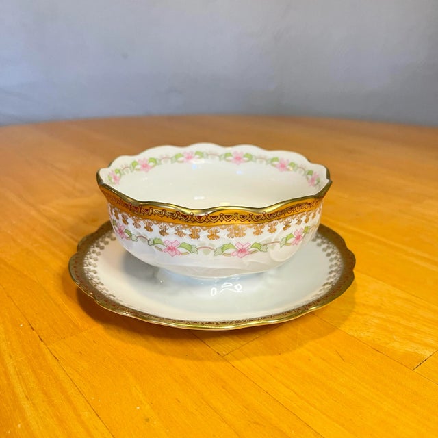 Hand painted trimmed in a gold scroll design with floral notes of pink and green. Under-plate is attached to bowl....