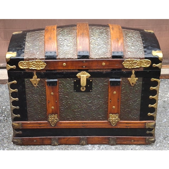This antique dome-top trunk, commonly referred to as a camelback or humpback chest, features embossed metal filigree...