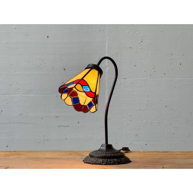Decorative Tiffany-style table lamp with a colored glass shade. The segmented glass with its geometric pattern in warm...