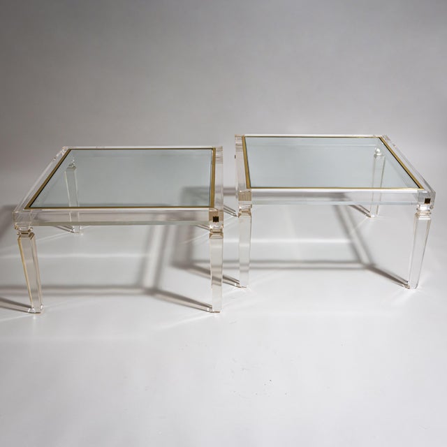 Pair of square coffee tables in clear acrylic glass with inset glass tops framed by brass surrounds. The tables retain the...