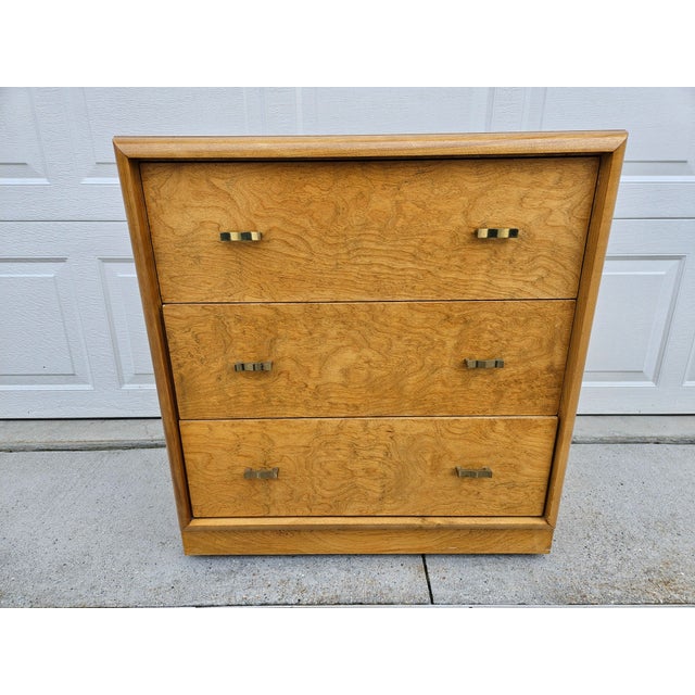 This three-drawer chest of drawers or small dresser features burlwood drawer fronts with brass-colored pulls. This piece...