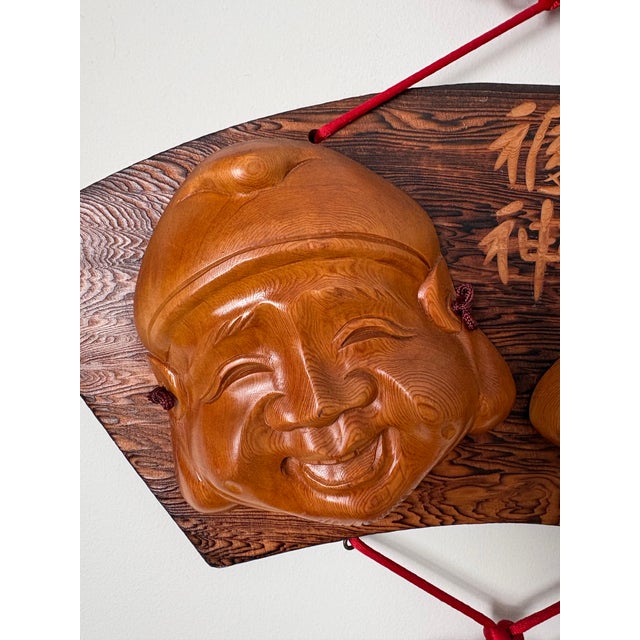 A decorative Japanese wall hanging featuring carved wooden masks of Ebisu and Daikoku, two of Japan’s Seven Lucky Gods...