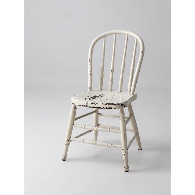 This vintage Windsor bow back chair features a beautifully worn cream-painted finish with delicate turned spindle...