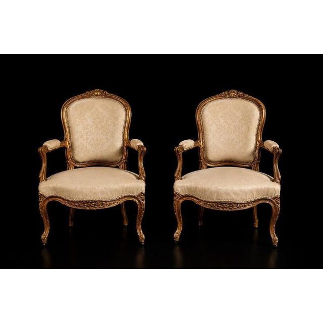 A refined pair of French Louis XV style fauteuil armchairs crafted in carved and gilt wood during the 19th century. The...