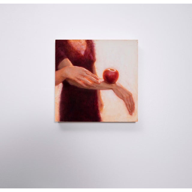 In "Before and Now Seems Infinite," a pair of delicate hands extends towards a glossy red apple resting on an arm,...