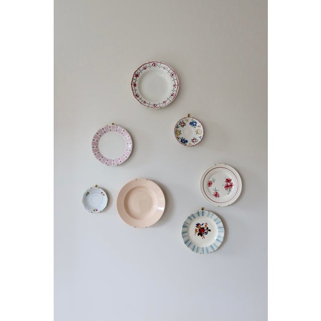 A decorative set of seven earthenware plates, united by a pink theme with floral and pastoral motifs. Each piece features...
