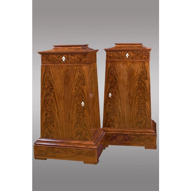 This pair of Danish mahogany cabinets of trapezoidal shape with drawer on top features a door with shelves and hidden...